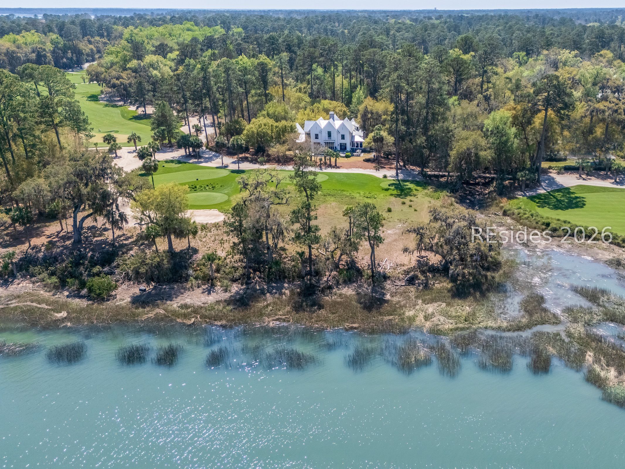White gabled home beside a golf course and waterway, viewed from above.