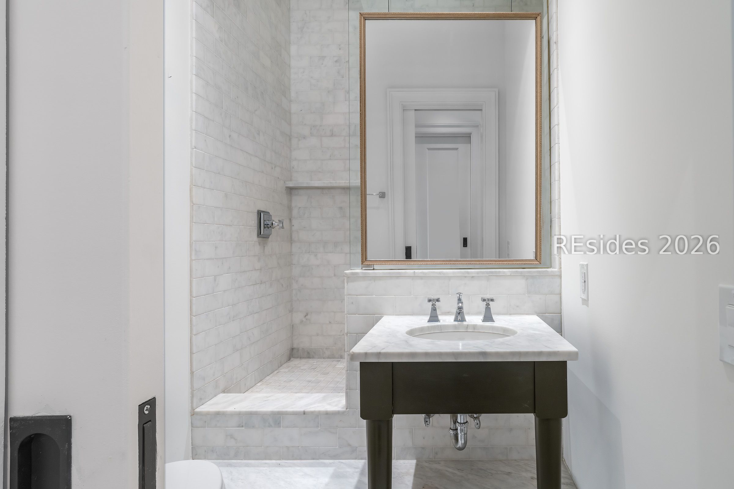Bathroom with a marble-tiled walk-in shower, marble vanity, and gold-framed mirror.