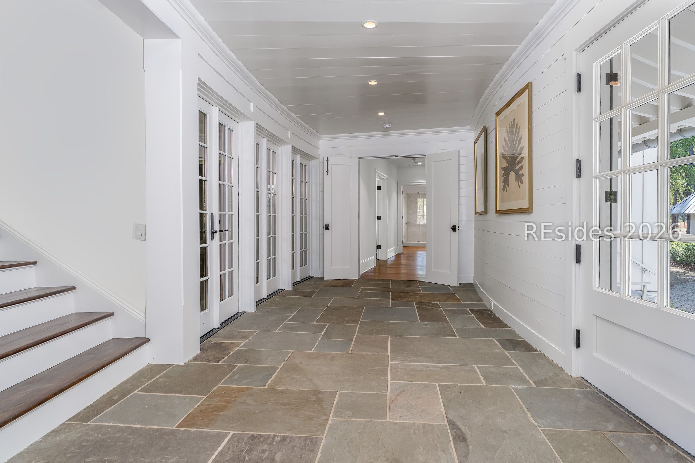 Entry hall with stone tile floors, white French doors, and a staircase along one side.