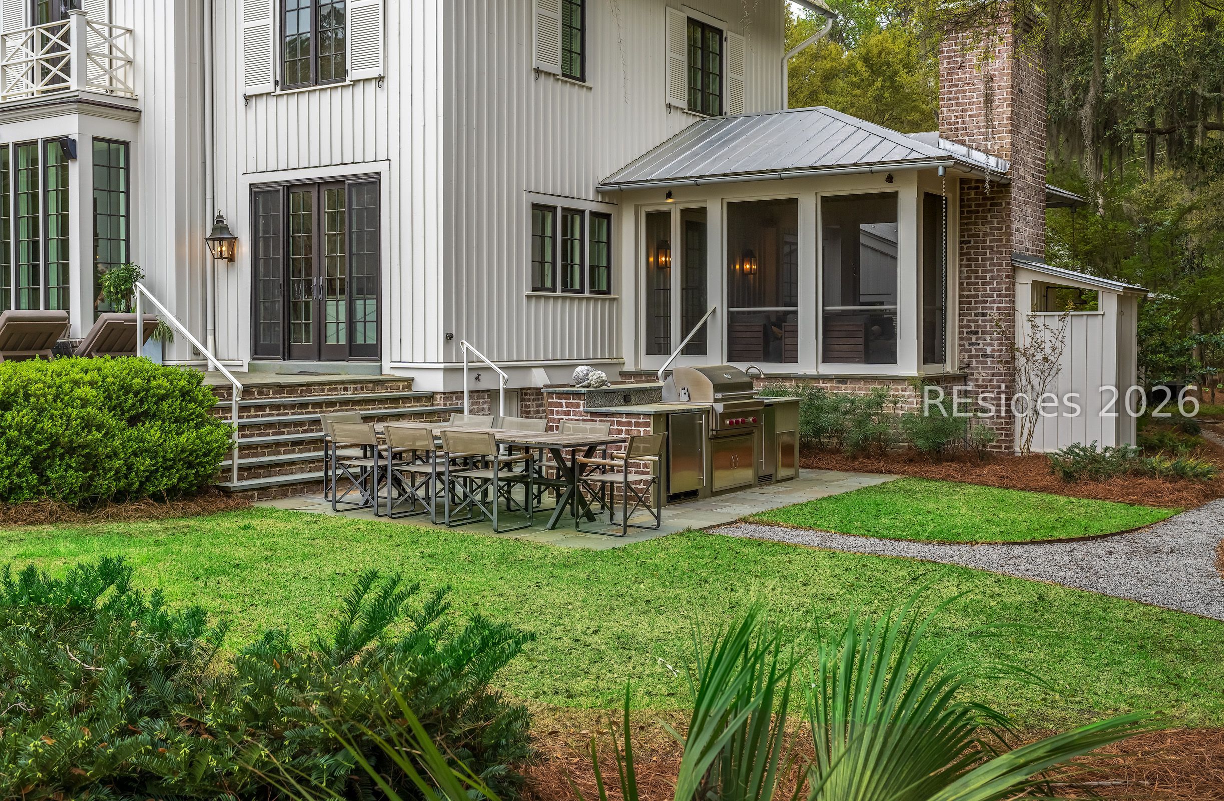 Home’s rear patio with a screened porch, outdoor dining table, and built-in grill.