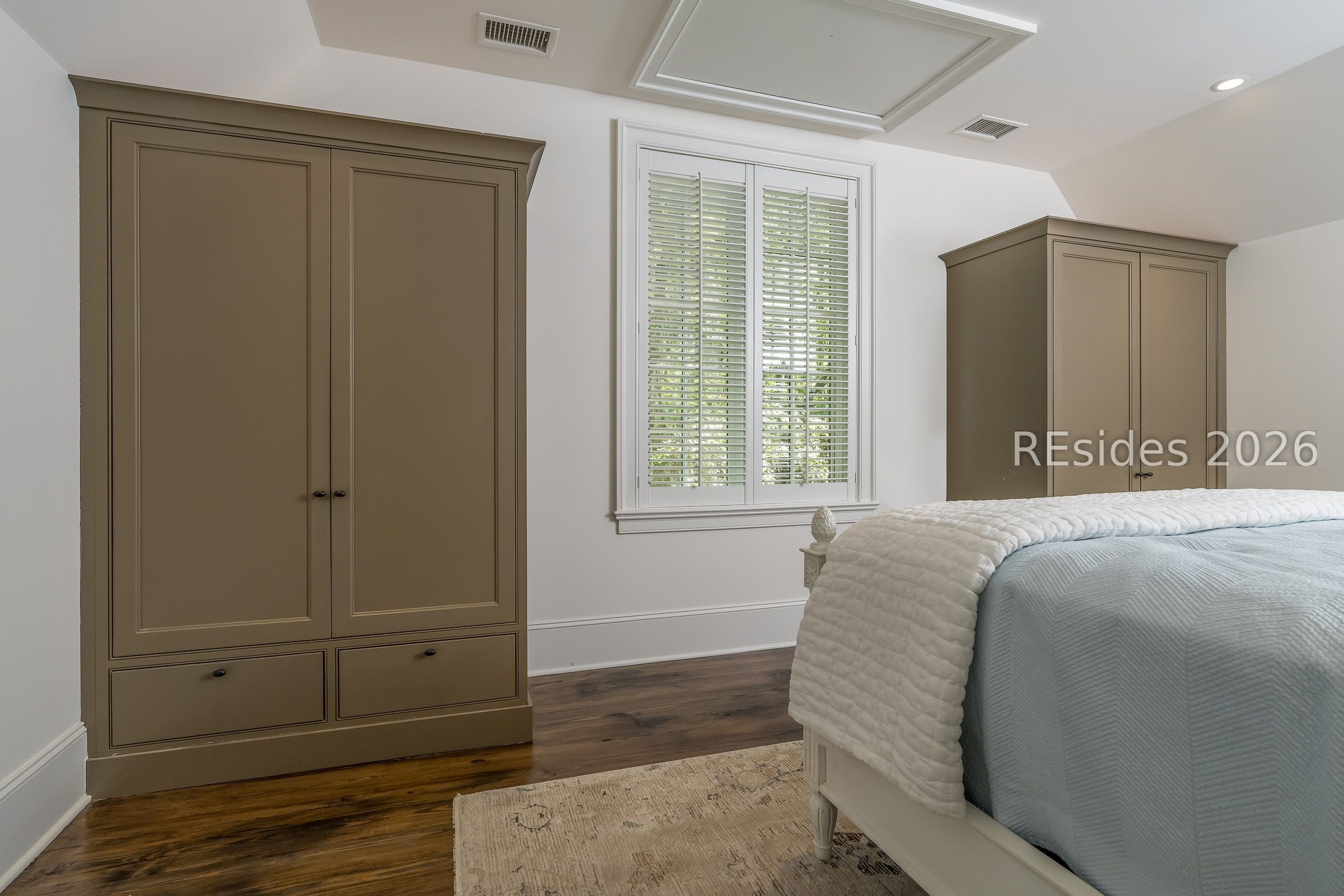 Bedroom with taupe built-in wardrobes, a shuttered window, and a white bed with pale blue bedding.