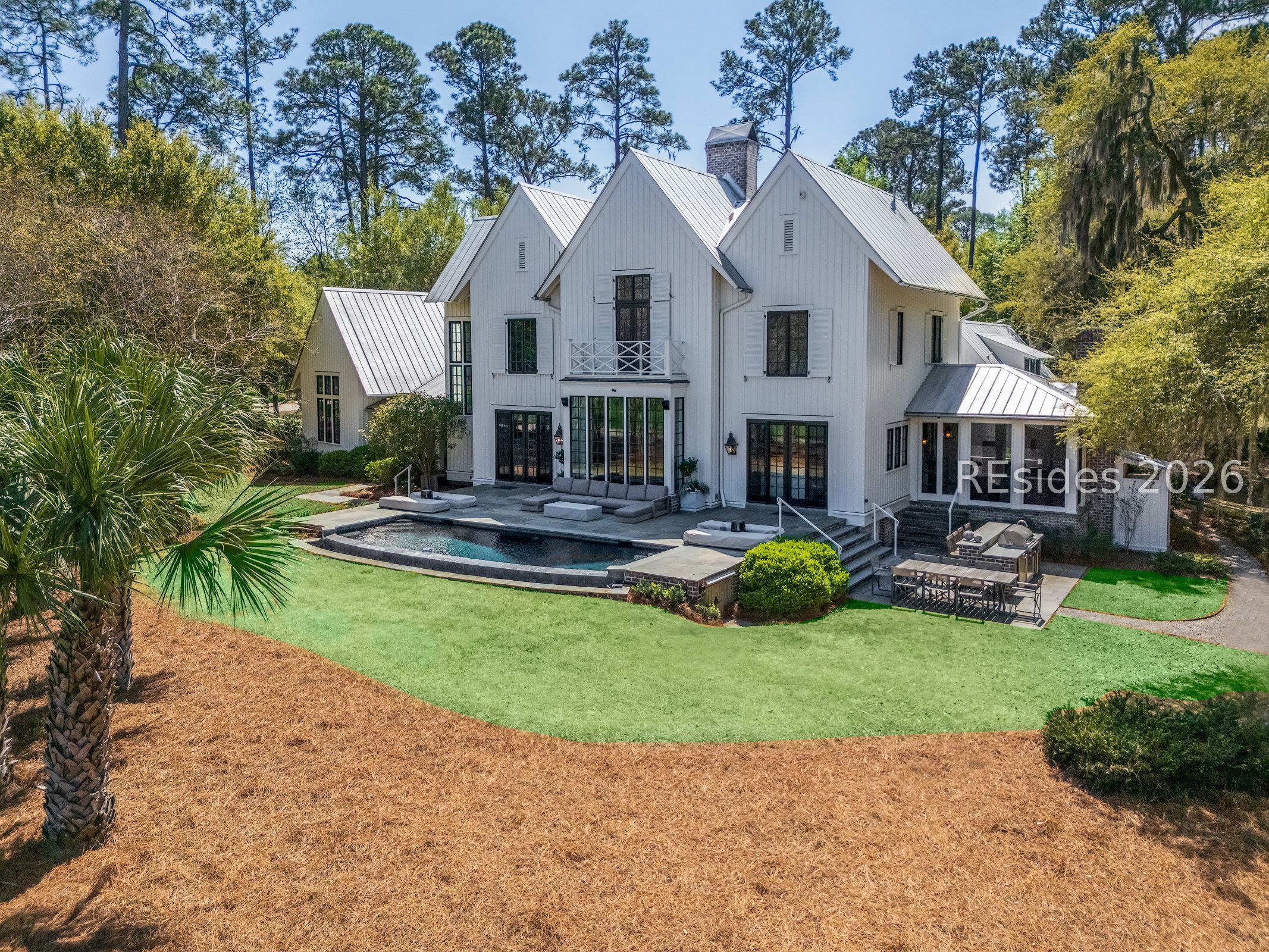 White two-story home with metal roof, swimming pool, patio, and landscaped lawn.