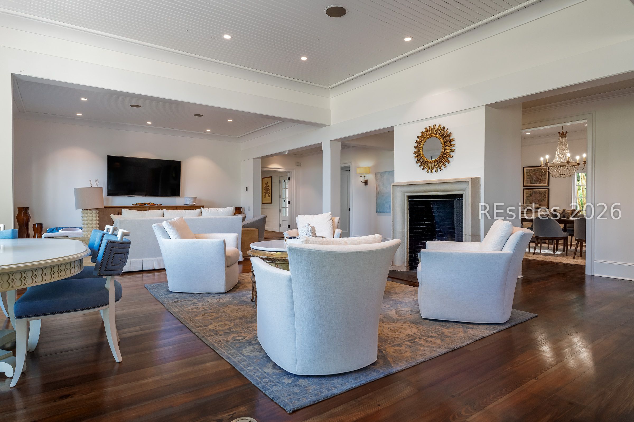 Living room with white seating, a fireplace, dark hardwood floors, and an adjoining dining room.