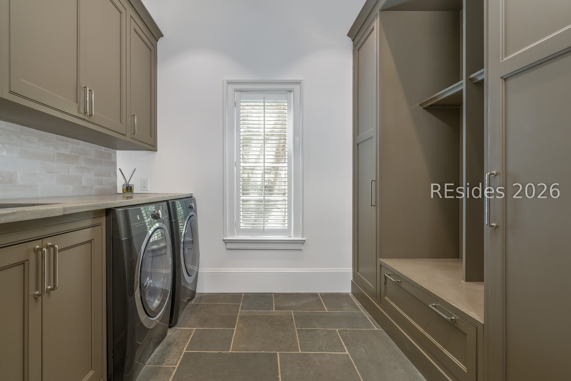 Laundry room with built-in cabinetry, front-loading washer and dryer, and a shuttered window.
