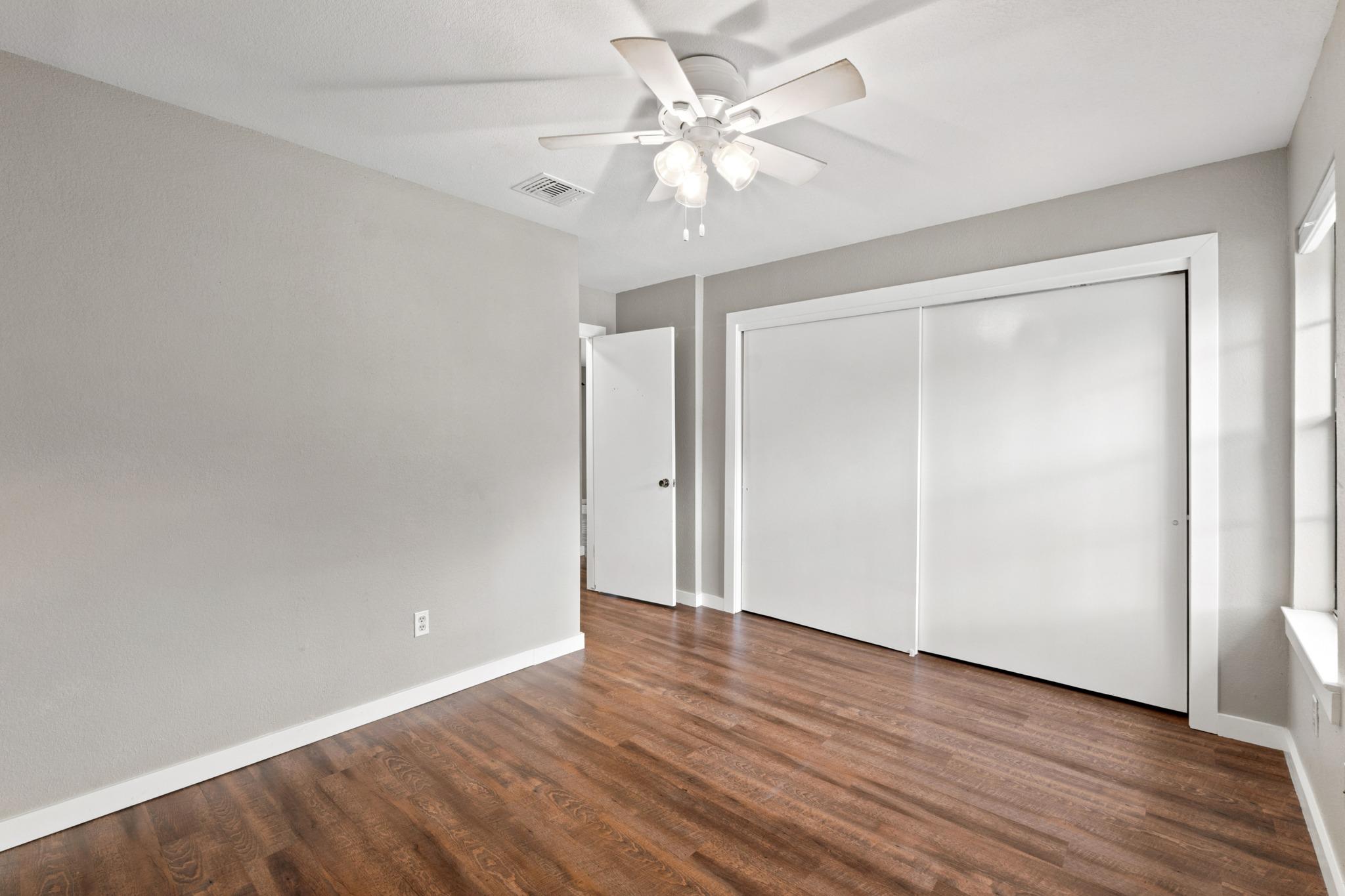 Empty bedroom with wood flooring, a ceiling fan, and a large sliding-door closet.