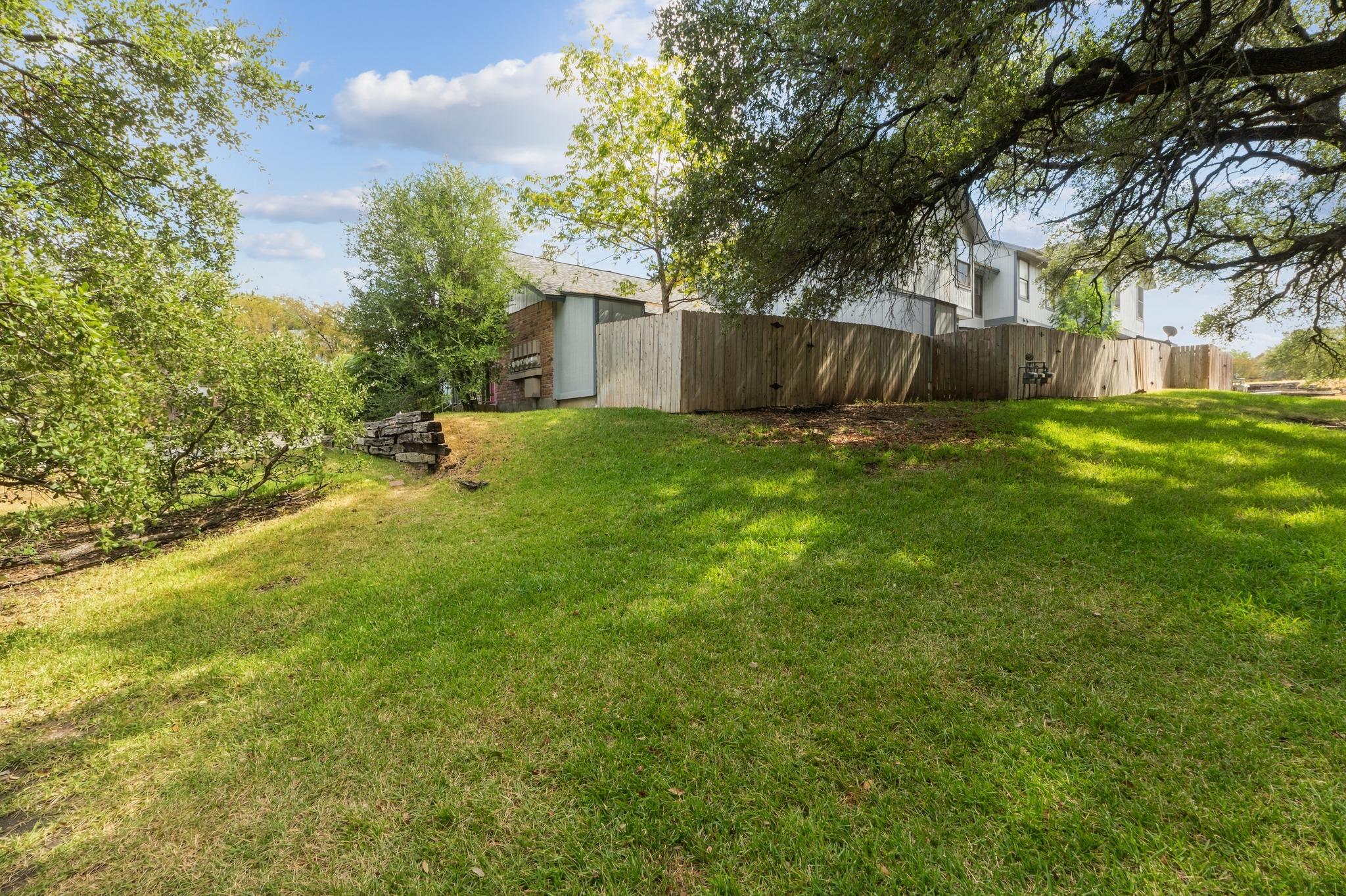 Townhouse behind a wooden privacy fence, bordered by a broad lawn and mature trees.