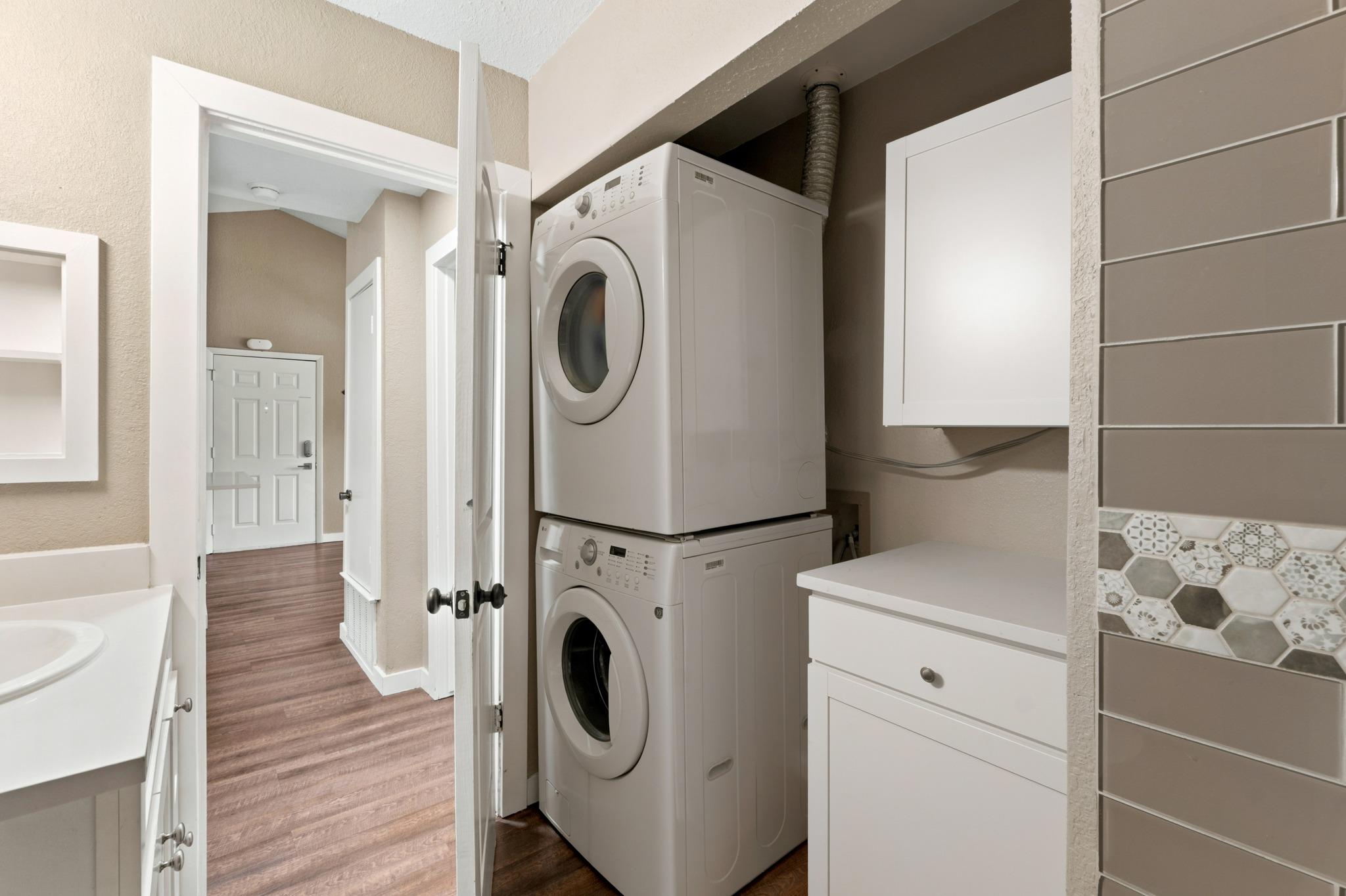 Laundry area with stacked washer and dryer beside white cabinetry and a patterned tile backsplash.