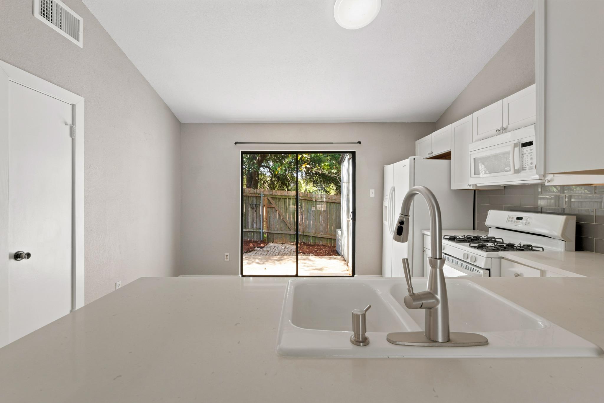 Kitchen with a large sink island, white appliances, and sliding doors to a fenced patio.