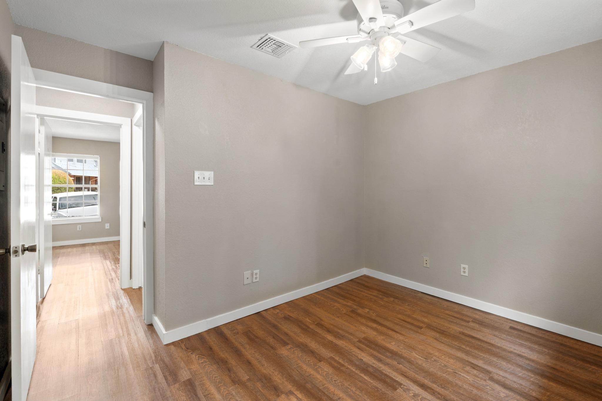 Vacant room with wood floors and ceiling fan, viewed through an open doorway to a second room.