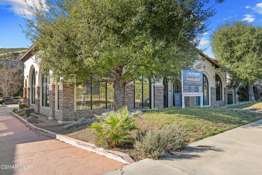 Commercial building with a stone facade, arched windows, mature trees, and an availability sign.
