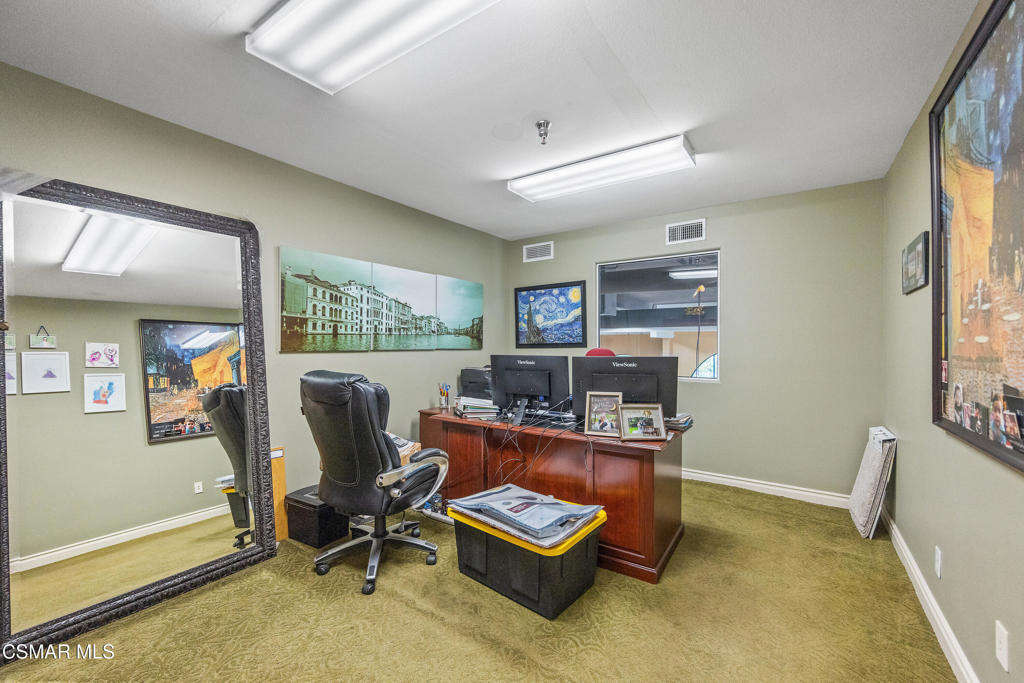 Home office with a wooden desk, dual monitors, and a large ornate floor mirror.