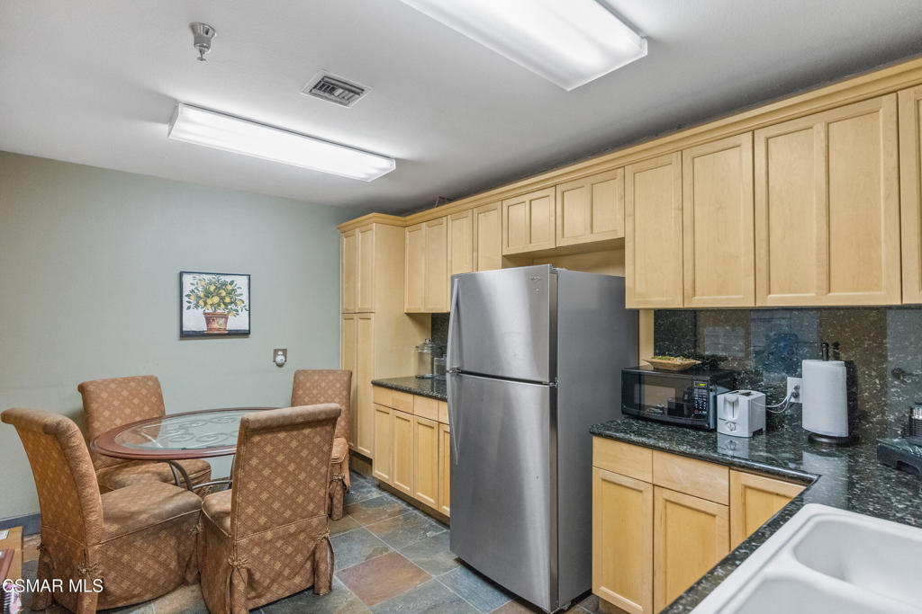 Compact kitchen with light wood cabinets, stainless-steel refrigerator, and round glass table with upholstered chairs.