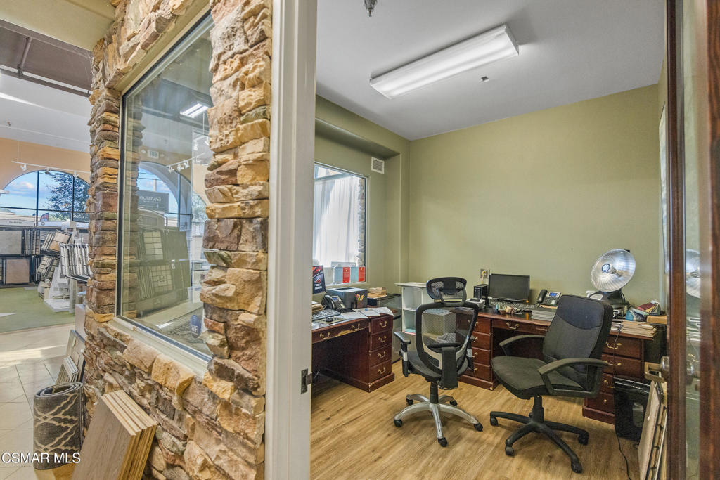 Office with two desks and rolling chairs, viewed through a stone-trimmed glass partition.