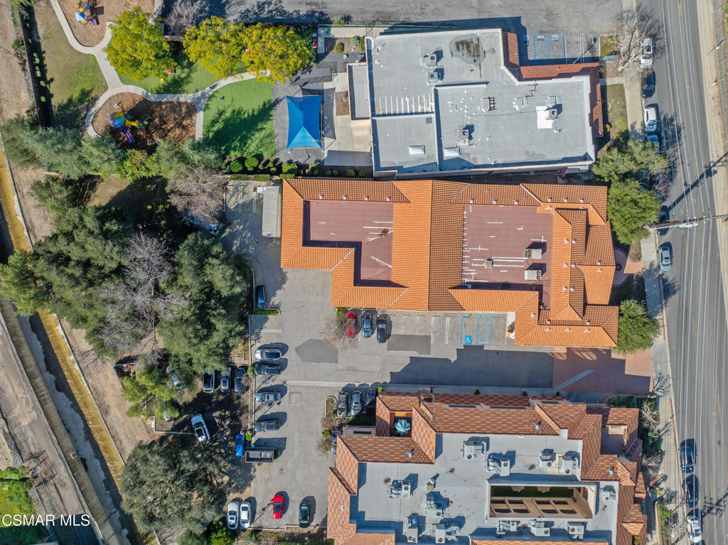 Aerial view of commercial buildings, parking areas, and landscaped grounds beside a road.