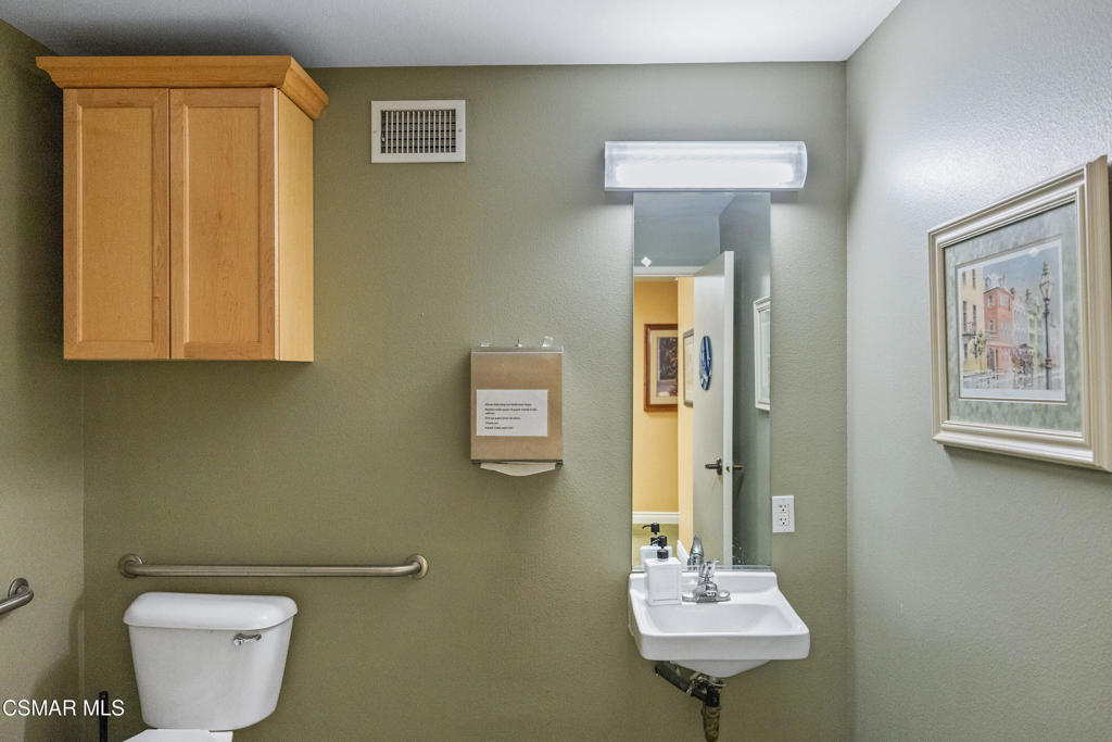 Bathroom with a toilet, wall-mounted sink, and grab bars beside the toilet.