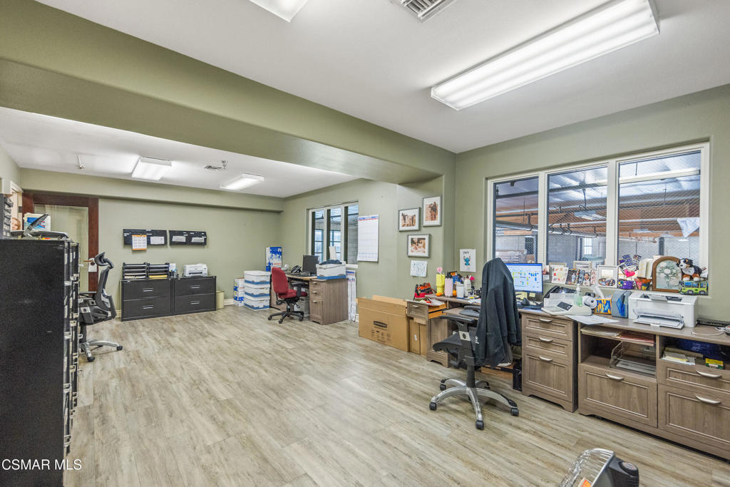 Office with several workstations, filing cabinets, and large windows overlooking a covered area.