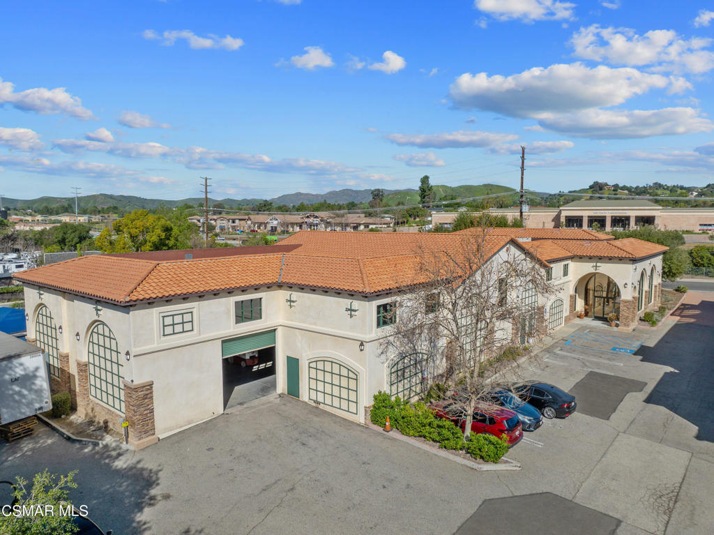 Aerial view of a cream commercial building with terracotta roofs, arched windows, and parking.