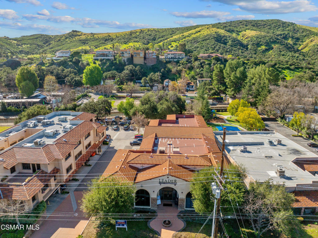 Aerial view of a tile-roofed commercial building, parking areas, and green hills.