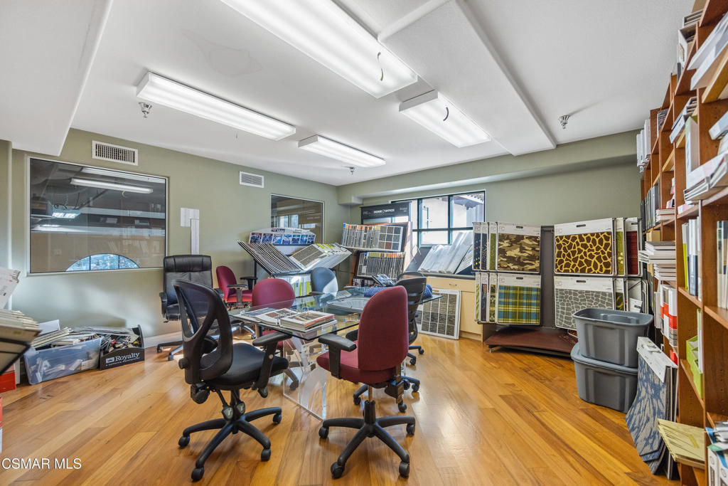 Office showroom with desks, chairs, flooring samples, and display shelving.
