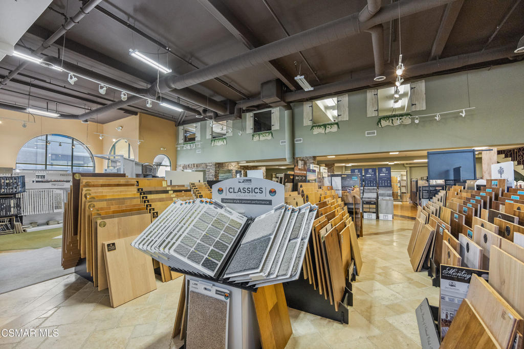 Flooring showroom with rows of wood, tile, and carpet samples beneath an exposed ceiling.