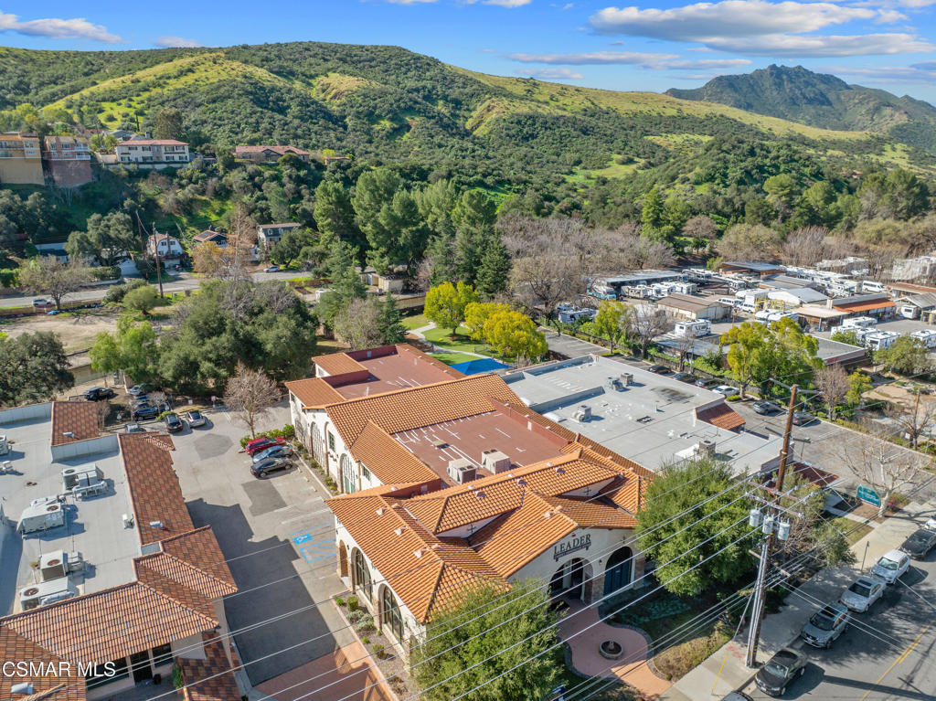 Aerial view of a terracotta-roofed commercial building with parking and green mountain hills beyond.