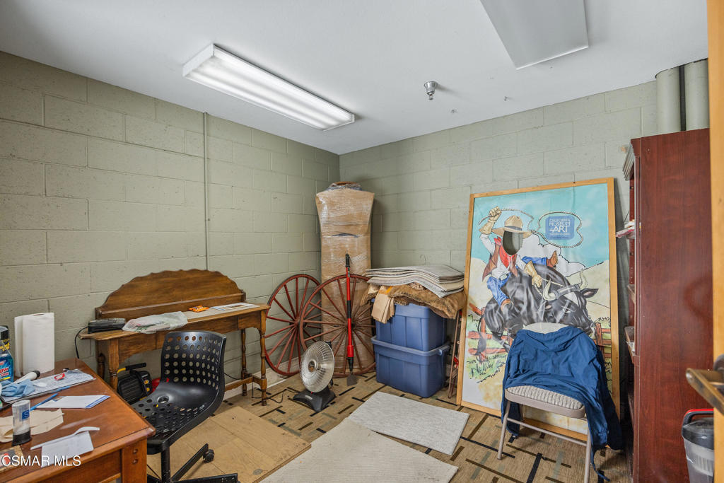 Office and storage room with cinderblock walls, desks, plastic bins, a wagon wheel, and a framed rodeo poster.
