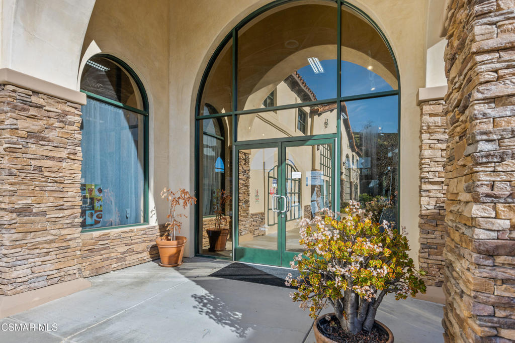Arched glass entrance framed by stacked-stone walls and potted plants.