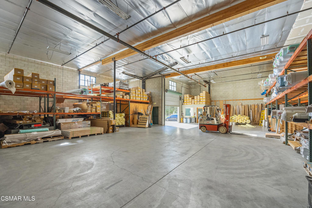 Warehouse interior with high beams, concrete floors, storage racks, building materials, and a forklift.