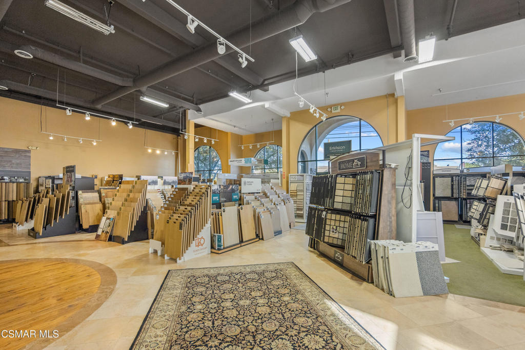 Flooring showroom with rows of wood, tile, and carpet samples beneath exposed ceilings.