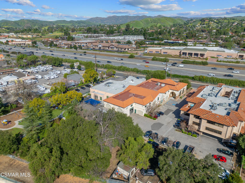 Aerial view of a commercial property with red tile roofs beside a freeway and green hills.