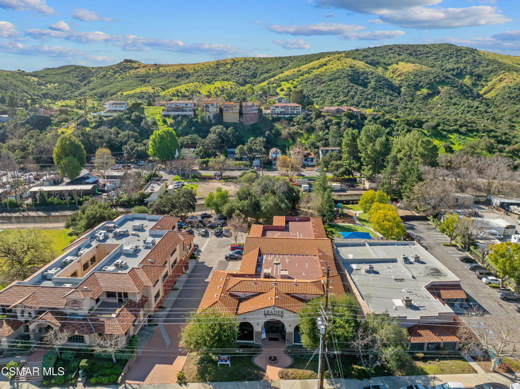 Aerial view of red tile-roofed commercial buildings and parking lots with green hills beyond.