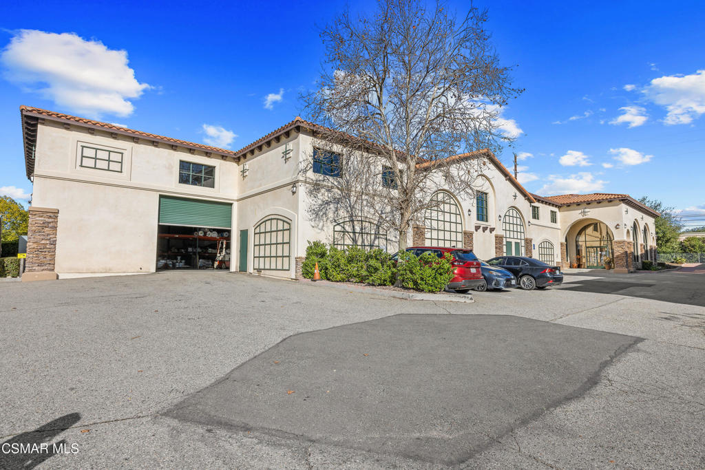 Two-story stucco property with arched windows, a tile roof, and a paved parking area.