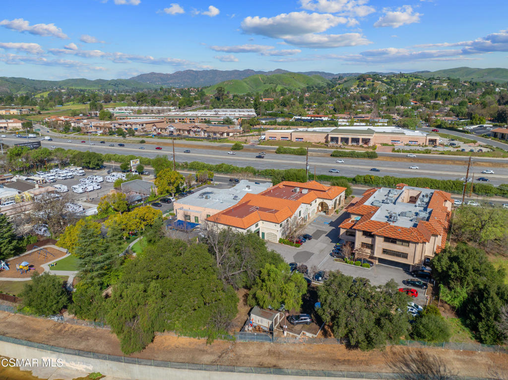 Aerial view of commercial buildings beside a highway, with green hills and mountains in the distance.