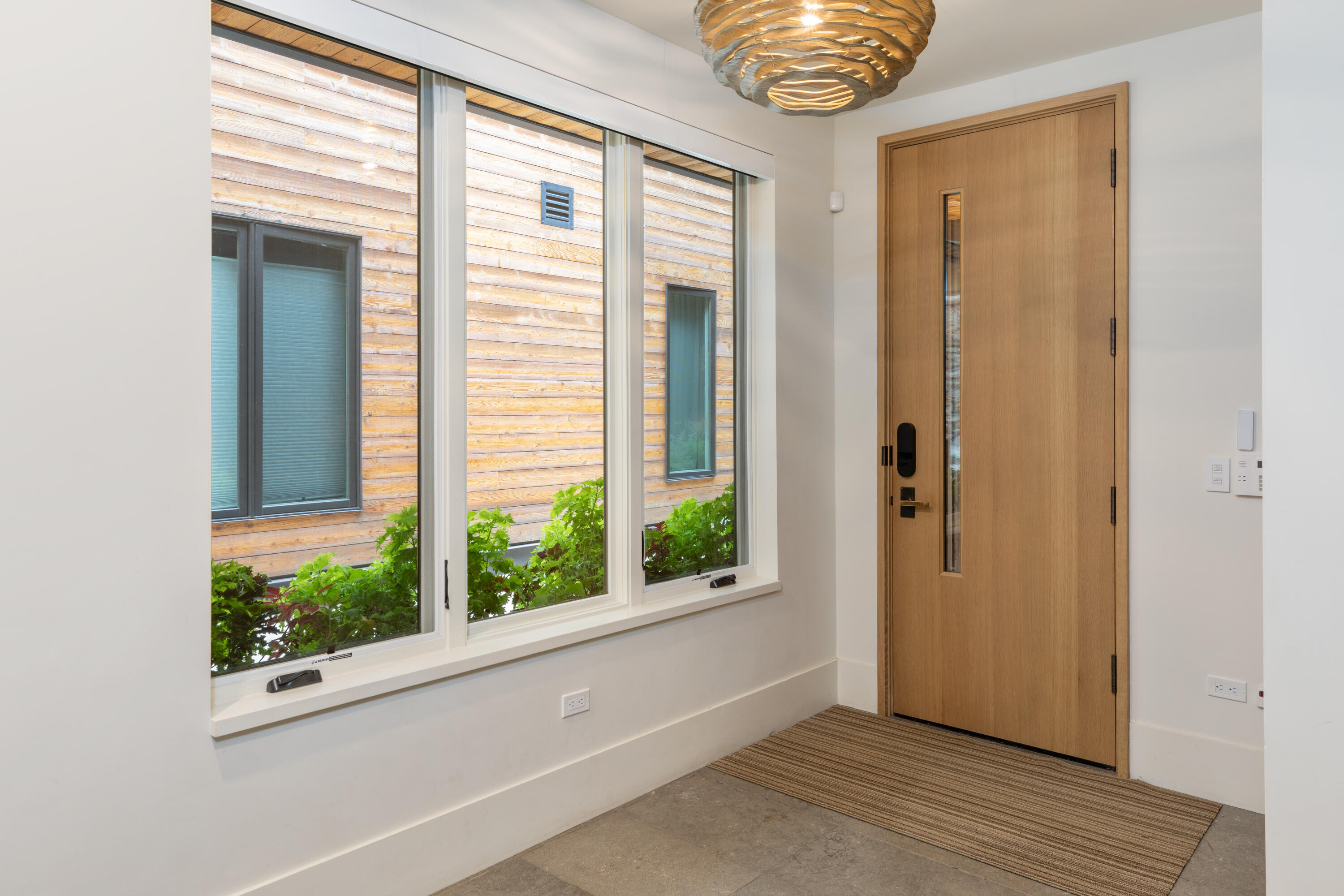 Modern entryway with a wood front door, tall windows, sculptural ceiling light, and striped rug.