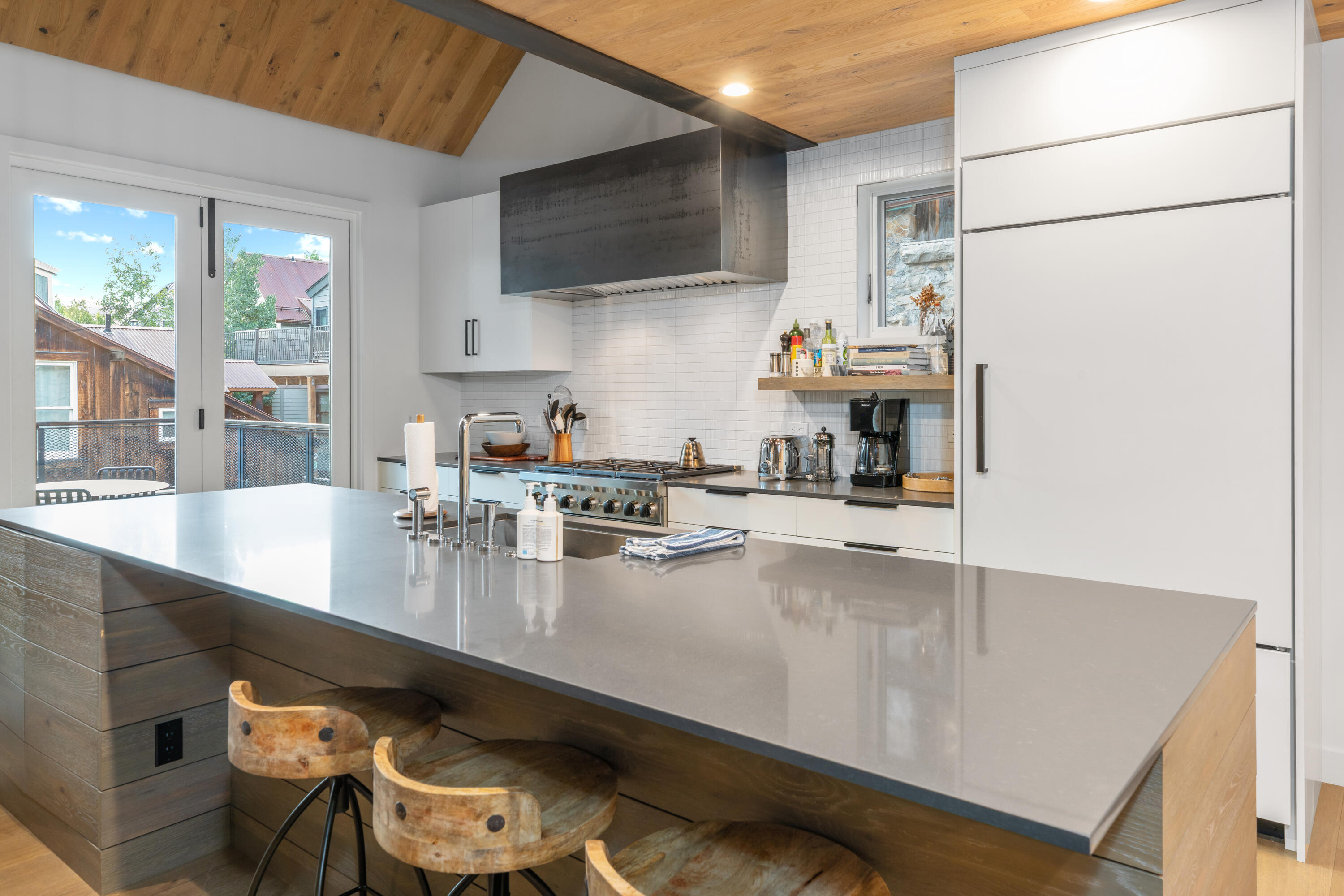 Modern kitchen with a large island, wooden stools, and vaulted wood ceiling