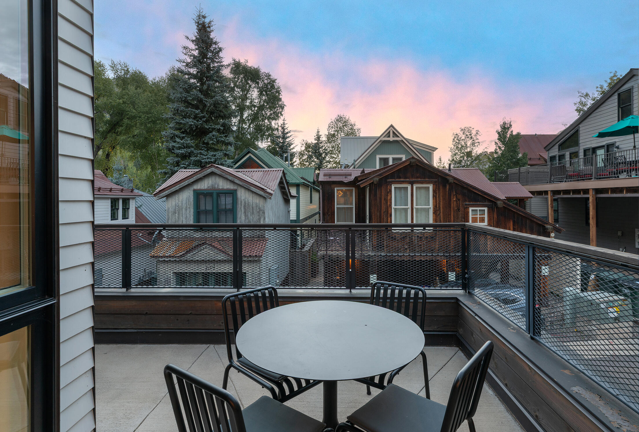 Deck with outdoor dining set overlooking neighboring rooftops at dusk.
