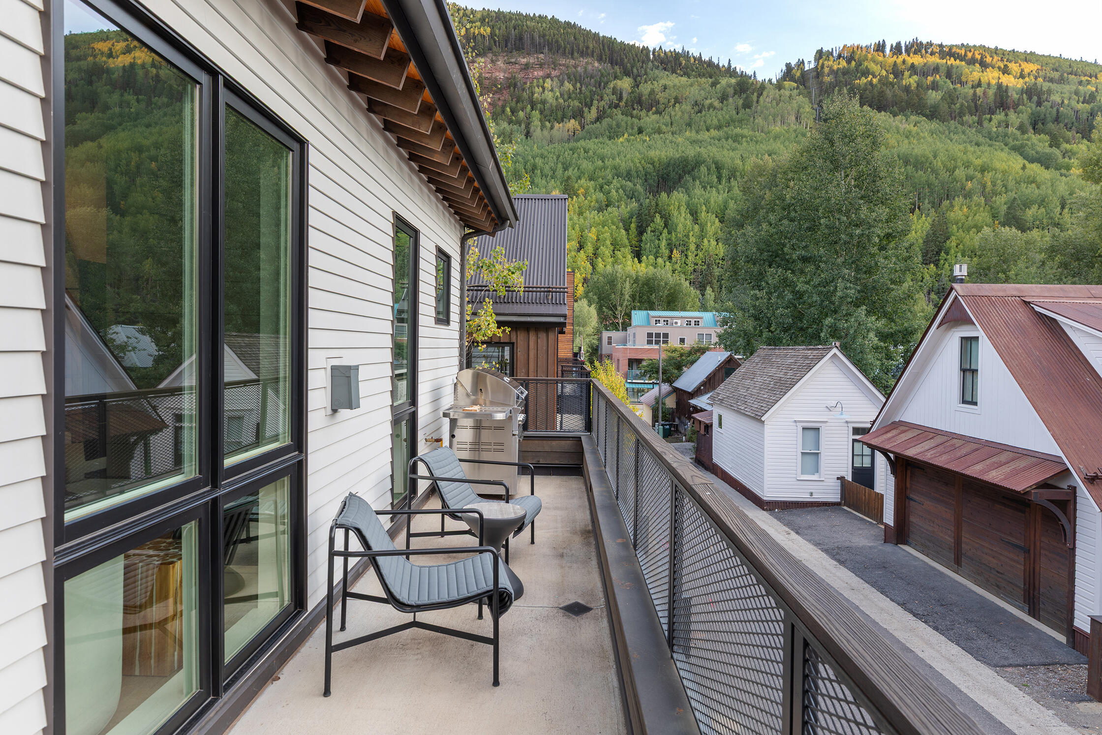 Condo balcony with lounge chairs and grill overlooking homes and an autumn mountain forest.
