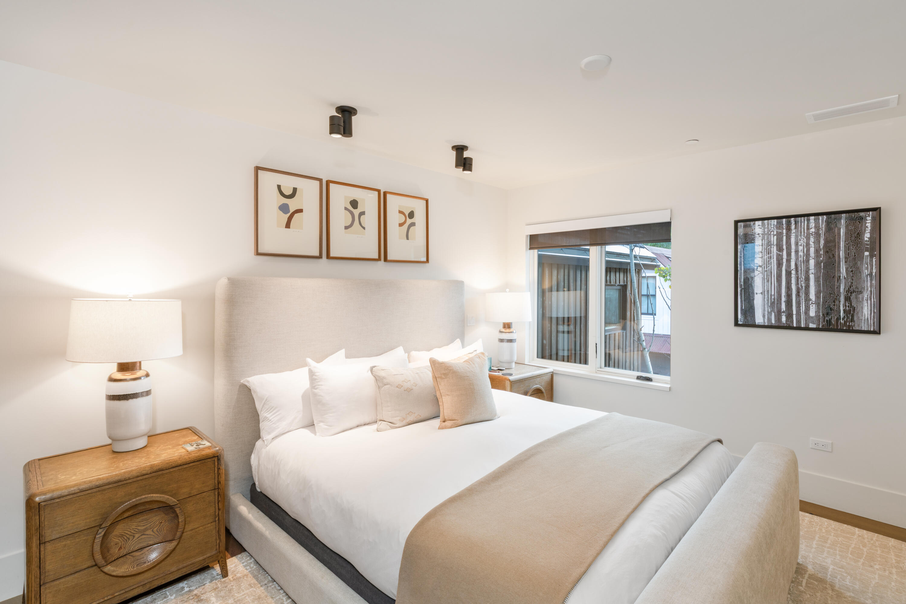 Staged bedroom with a white bed, upholstered headboard, wooden nightstands, and framed artwork.