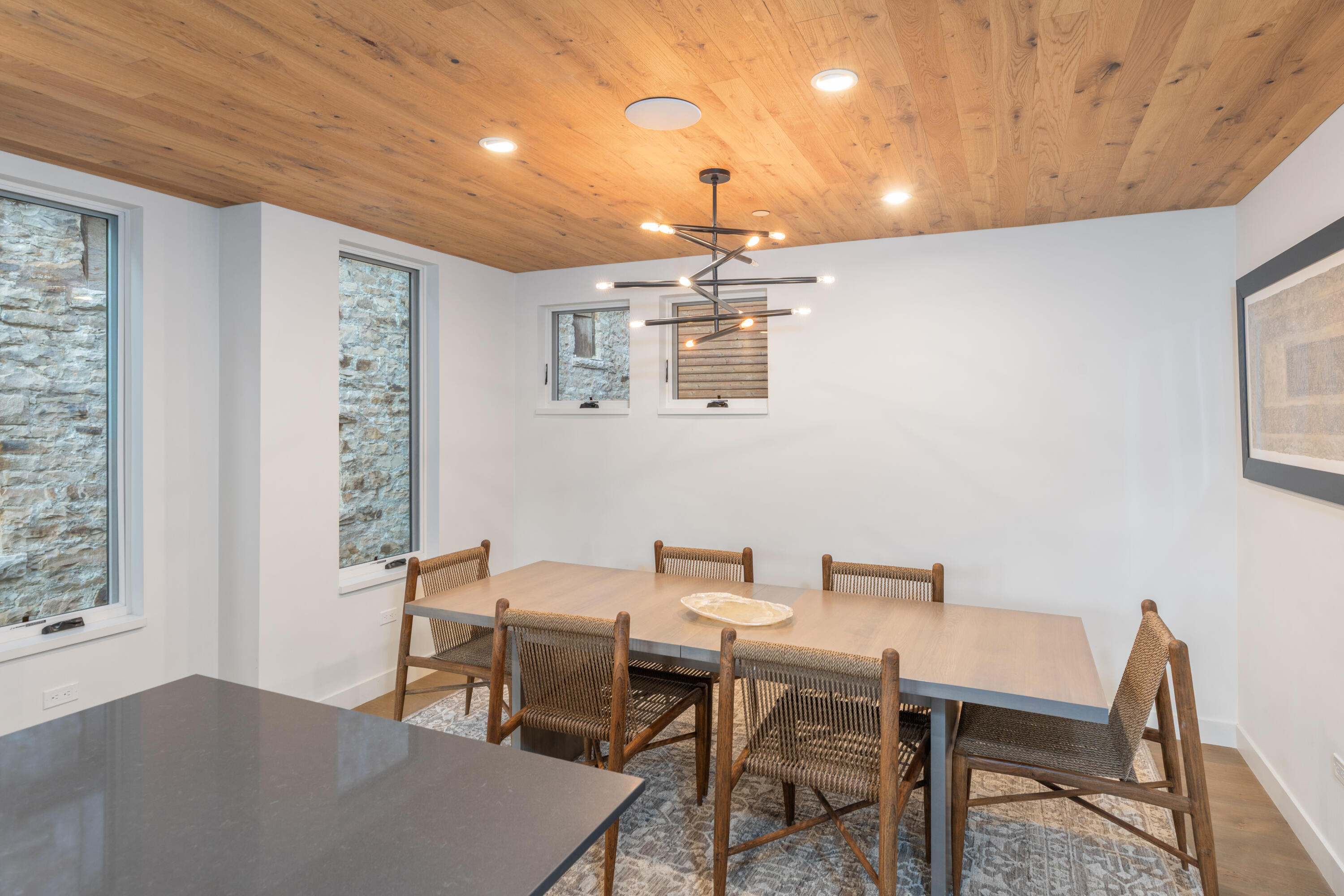Dining room with woven chairs, a long table, and a warm wood-plank ceiling.