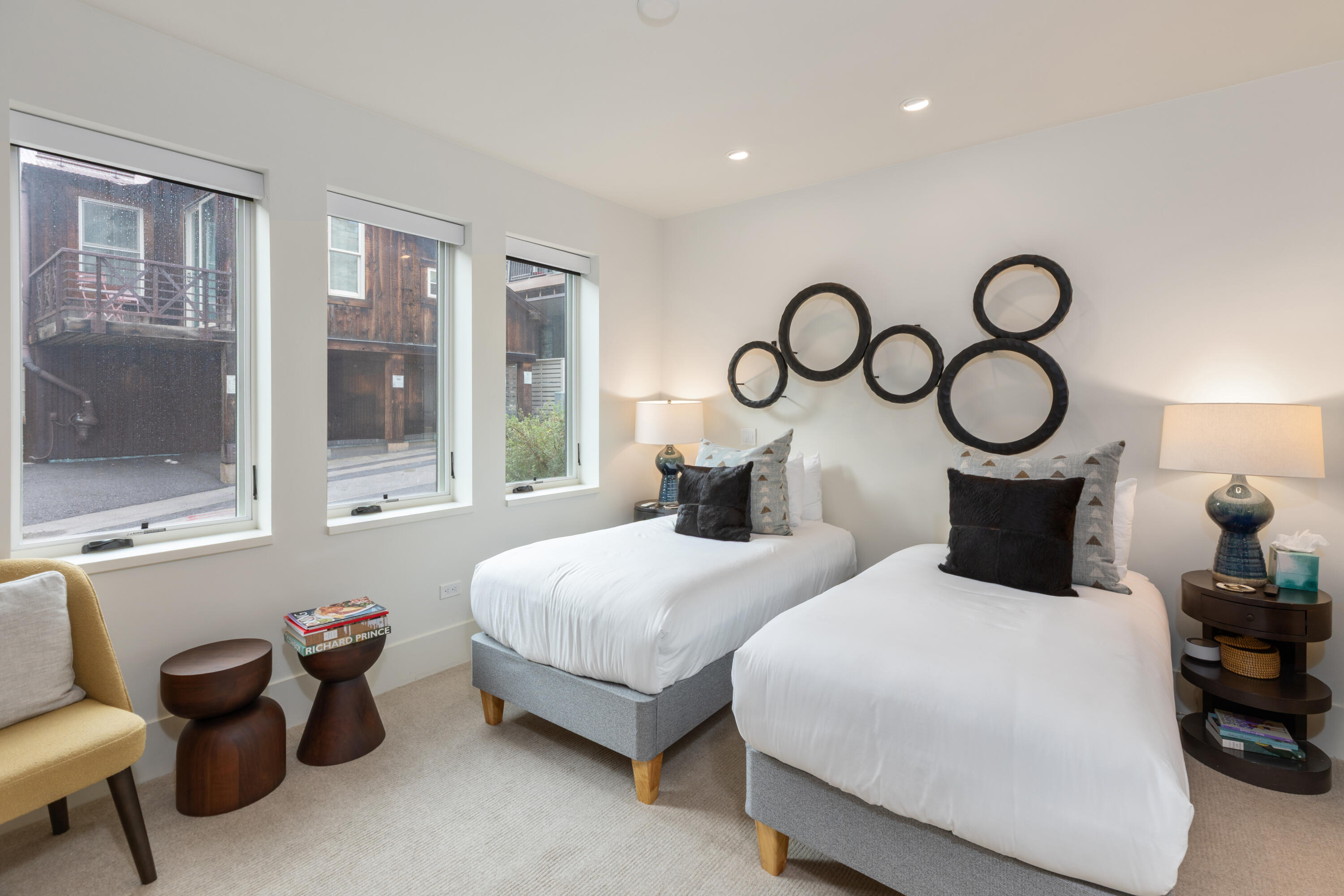 Bedroom with two white beds, circular black wall decor, and three tall windows.