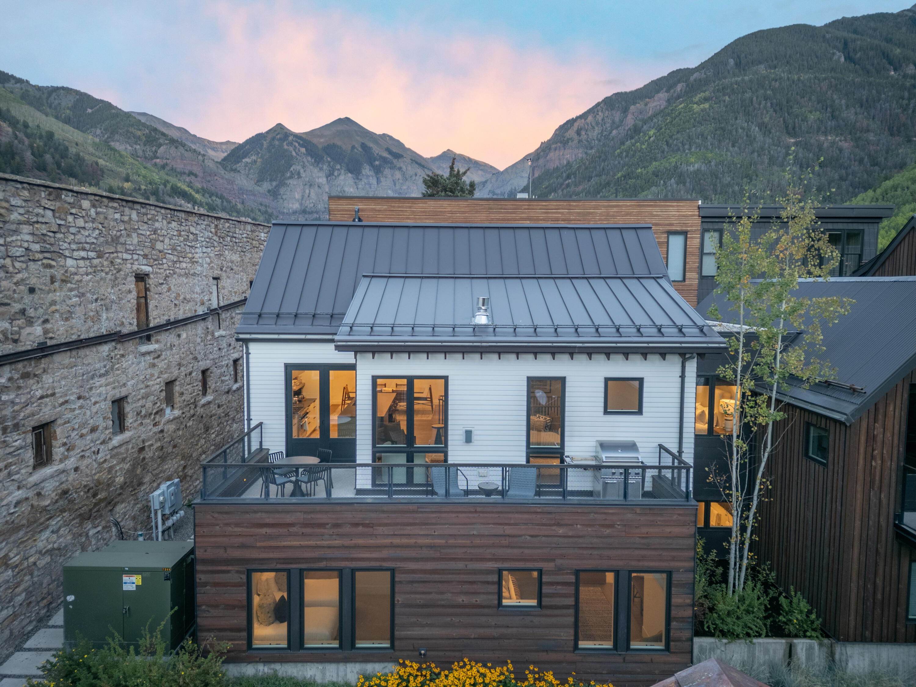 Modern Telluride home with a metal roof and raised deck beneath mountain peaks at dusk.