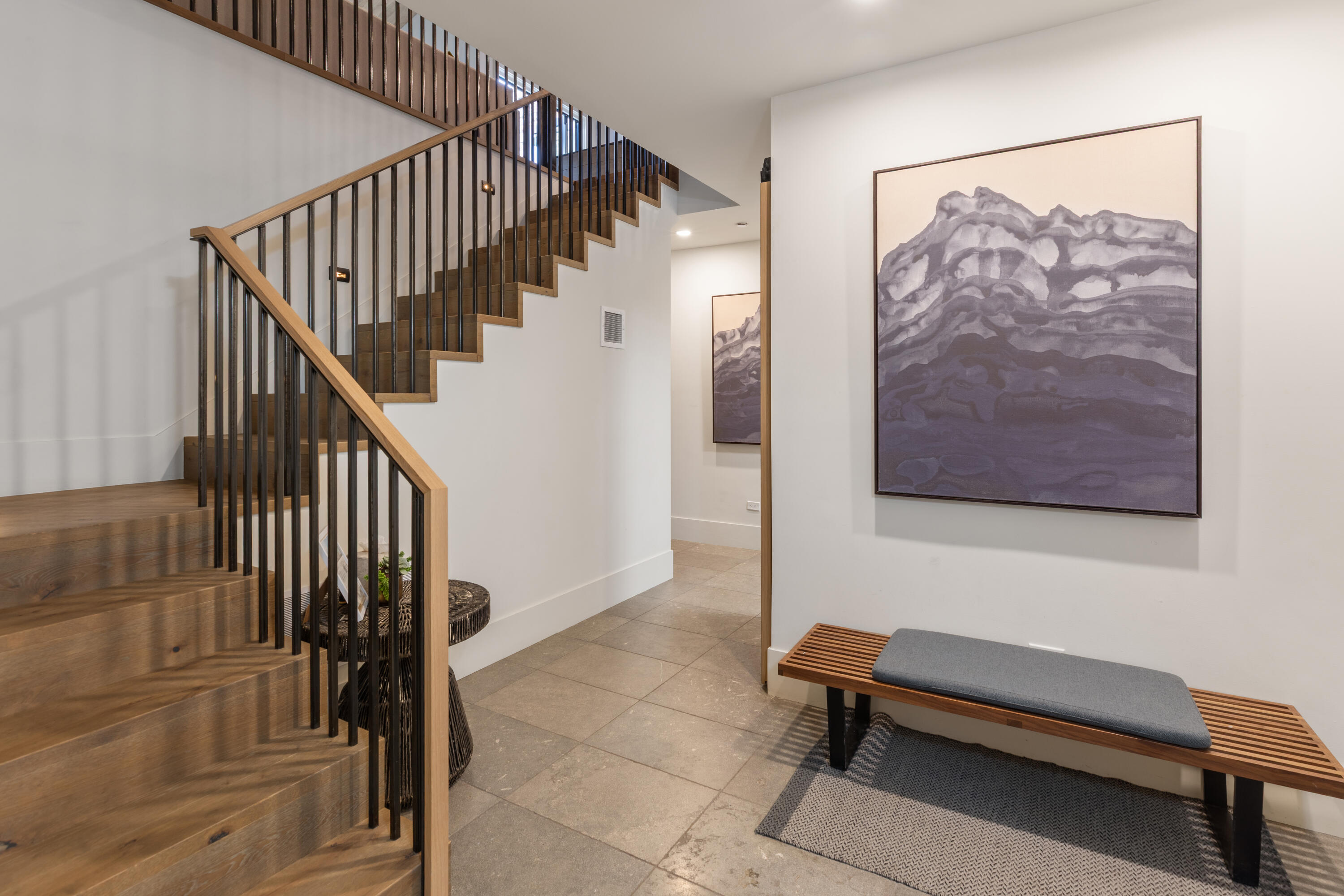 Entryway with a wood staircase, stone tile floor, and a bench beneath mountain artwork.