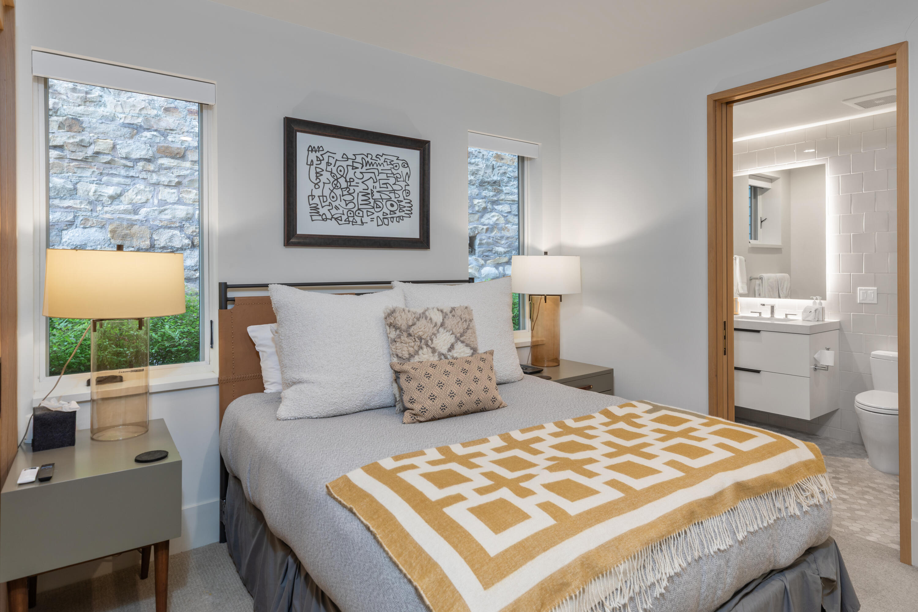 Bedroom with a gray bed and mustard geometric throw beside an ensuite bathroom.