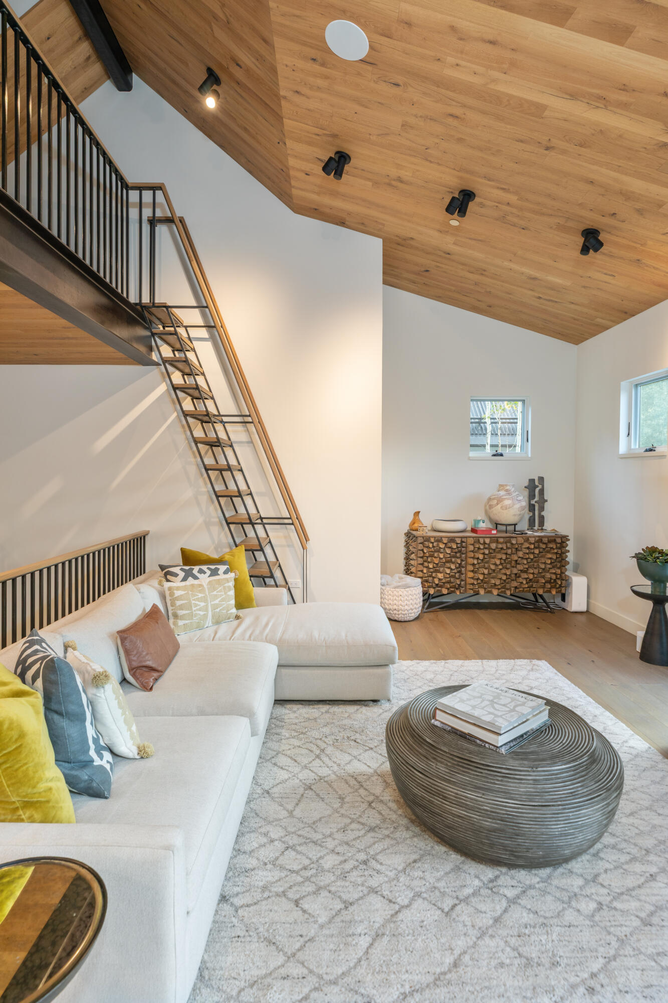 Living room with a vaulted wood ceiling, open loft staircase, white sectional, and round coffee table.