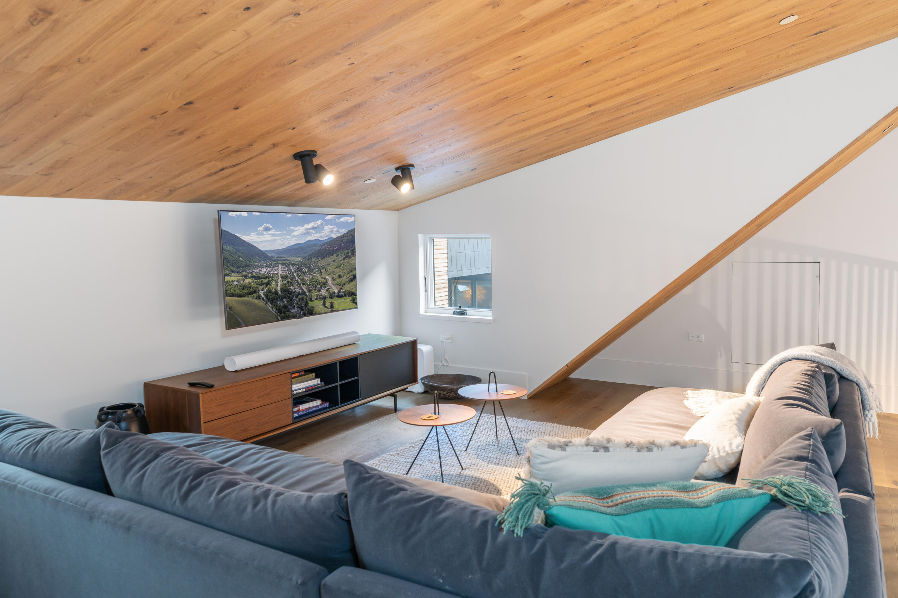 Living room with a gray sectional, turquoise pillow, wood ceiling, and diagonal ceiling beam.
