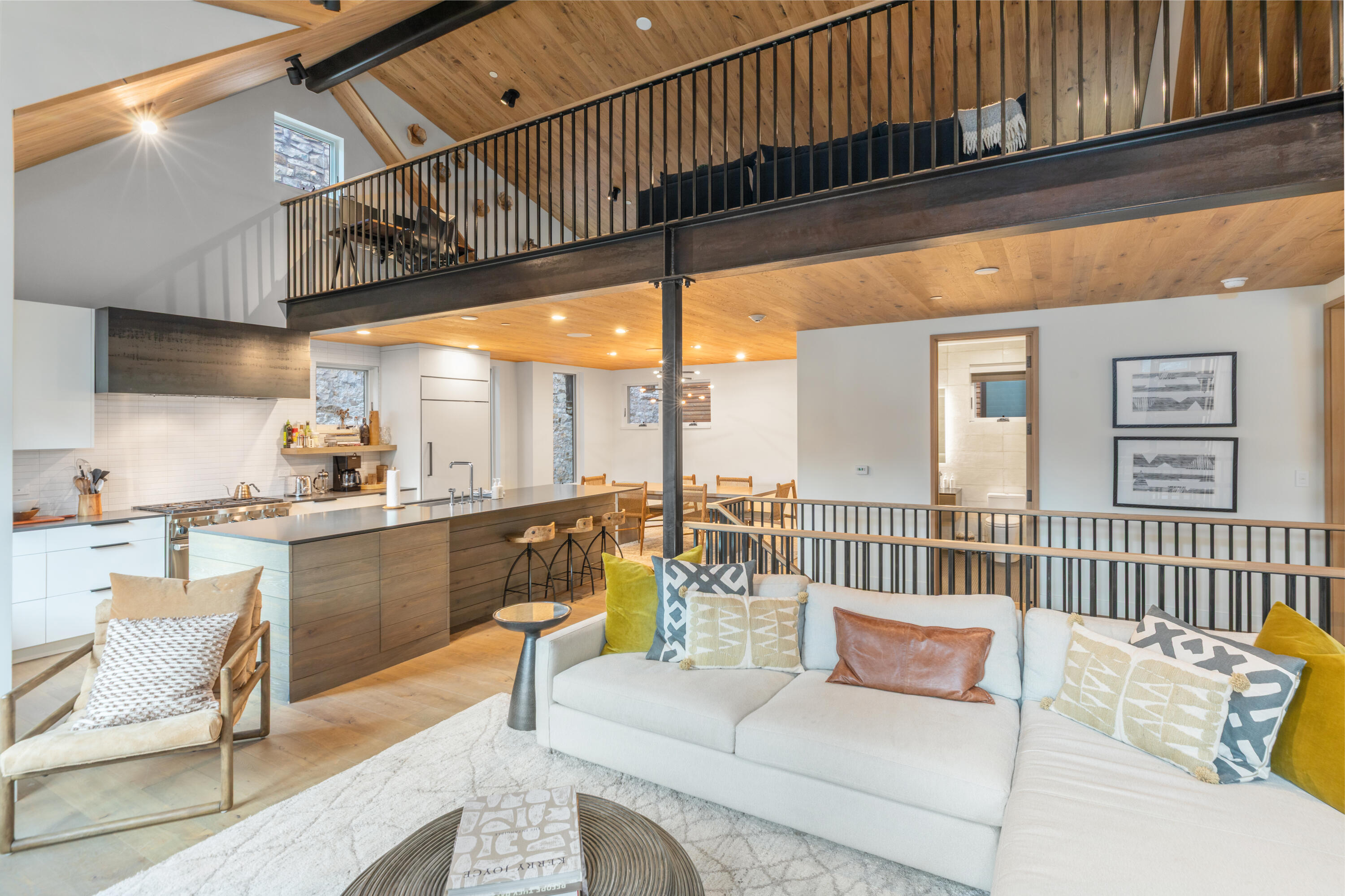Open-plan living room and kitchen with a white sectional, wood island, and black-railed mezzanine.