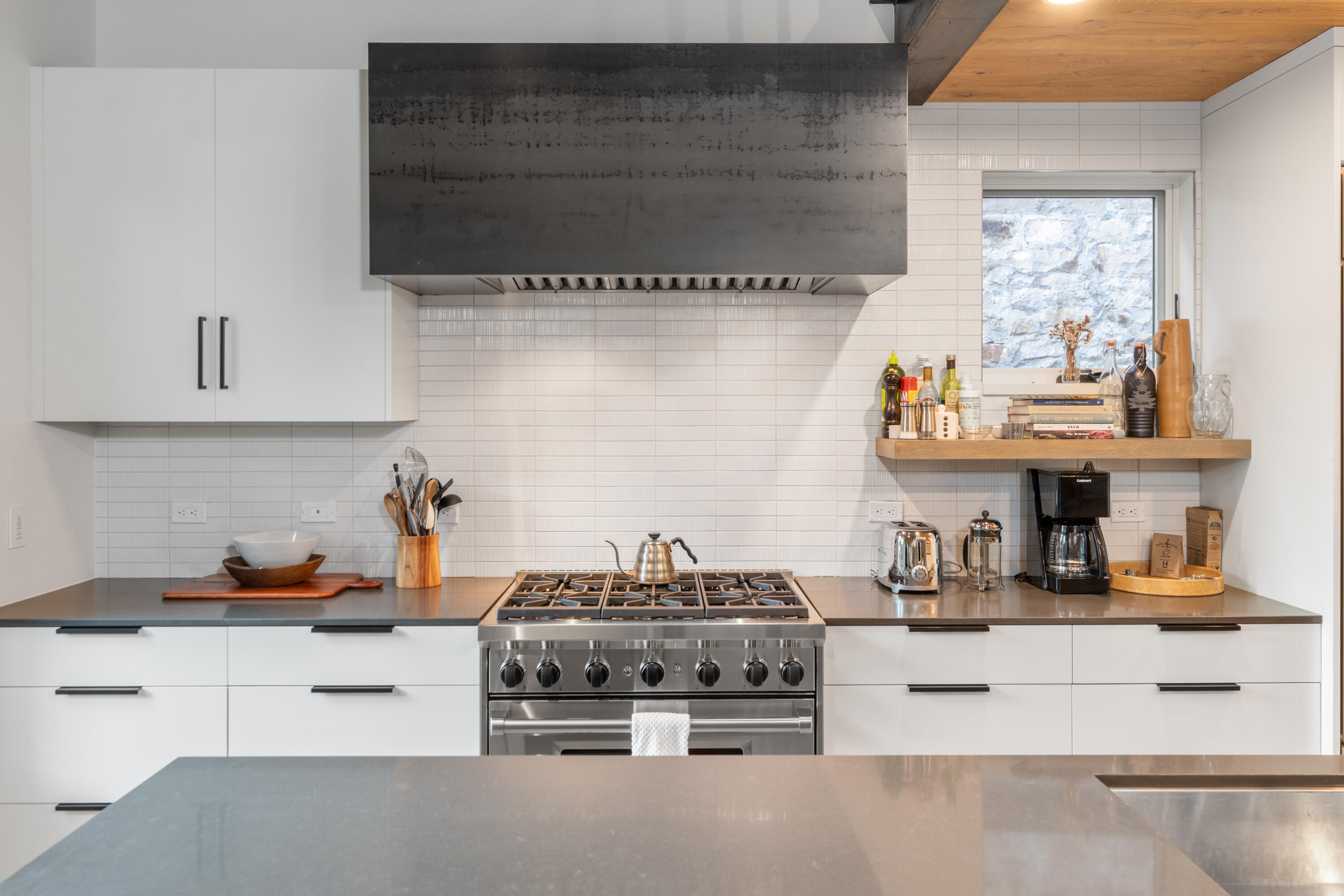 Modern kitchen with a stainless-steel range, oversized metal hood, and gray island.