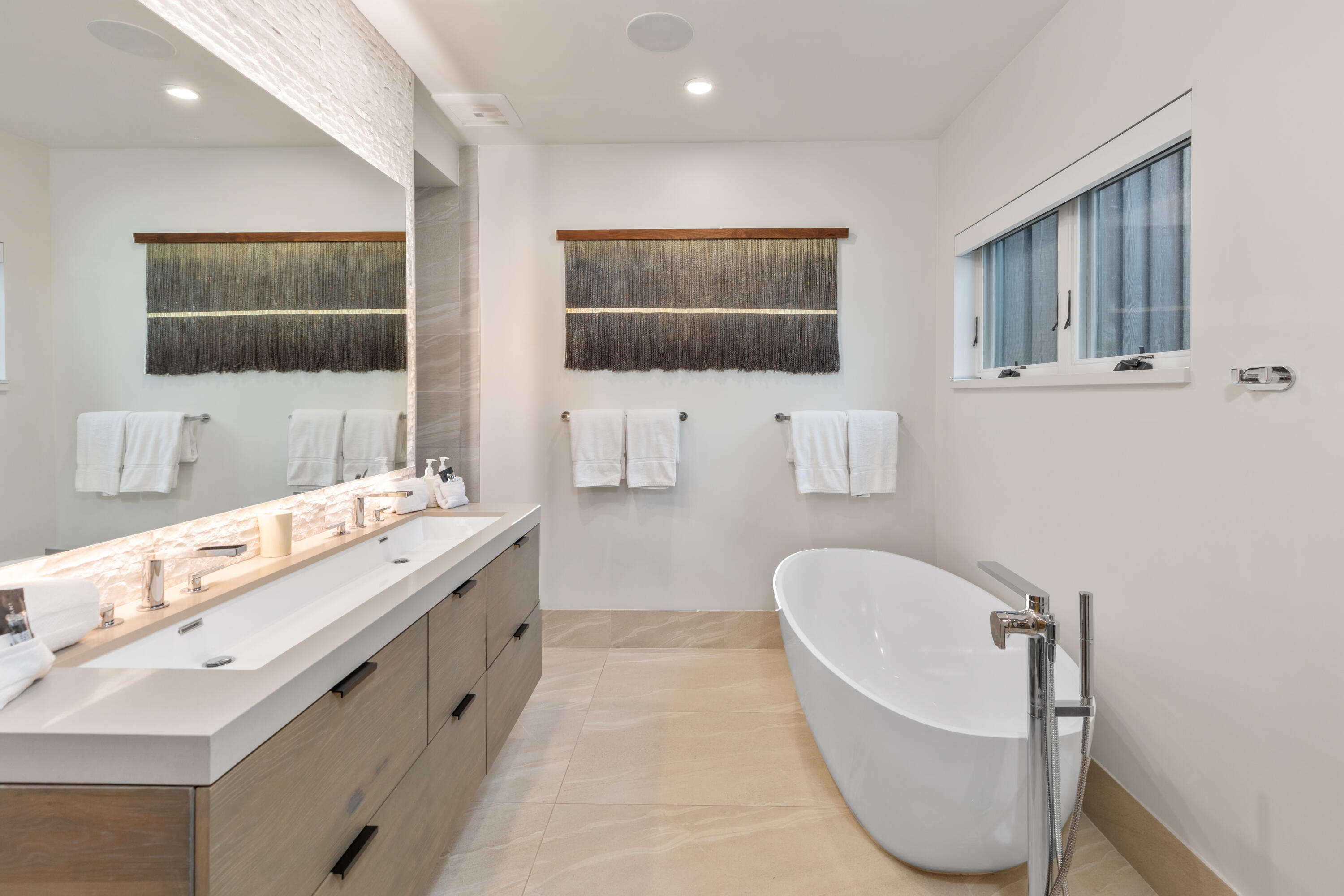 Modern bathroom with a freestanding soaking tub and long double vanity beneath a large mirror.