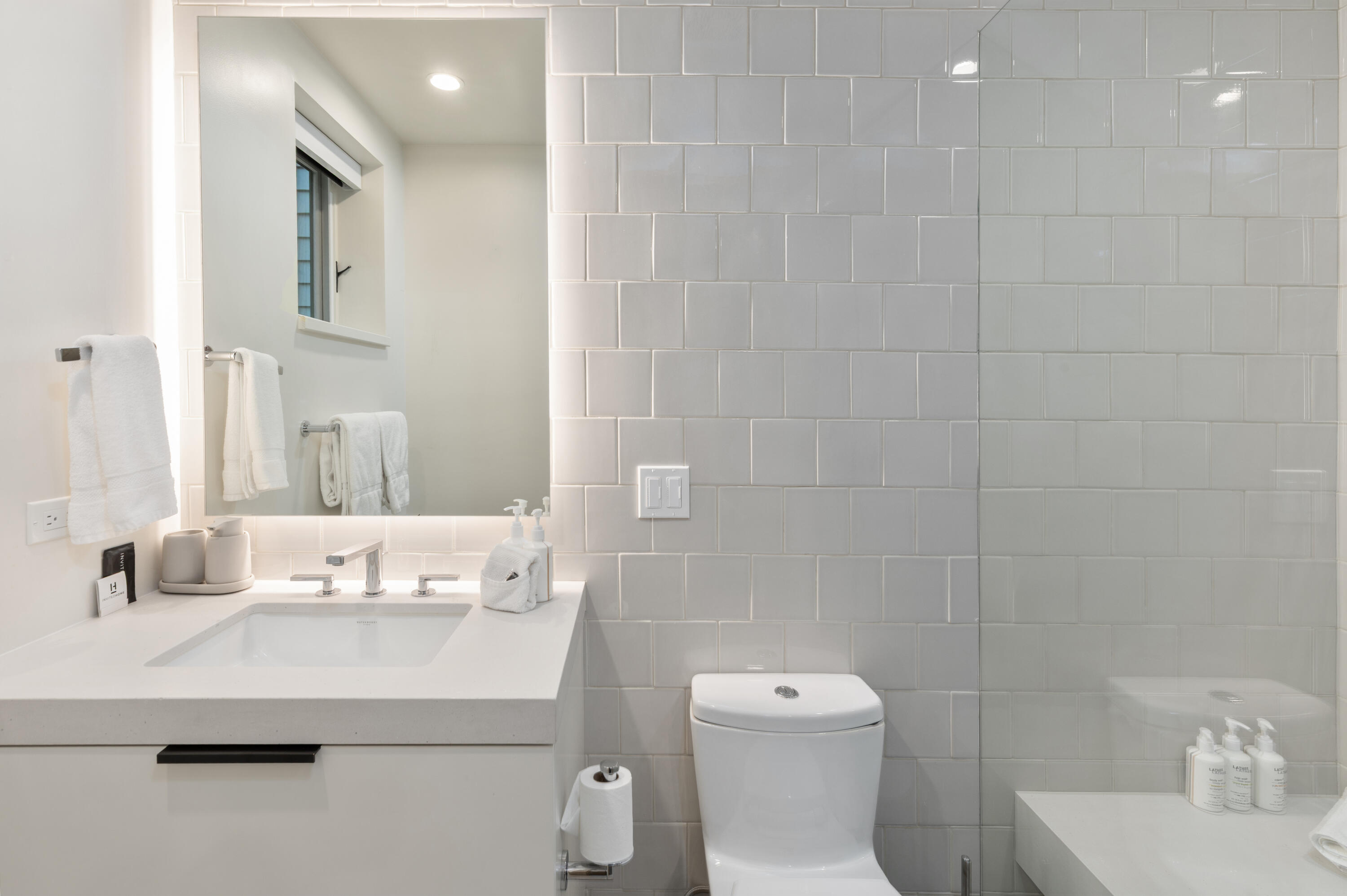 Modern bathroom with a white vanity, subway tile, toilet, and bathing area.