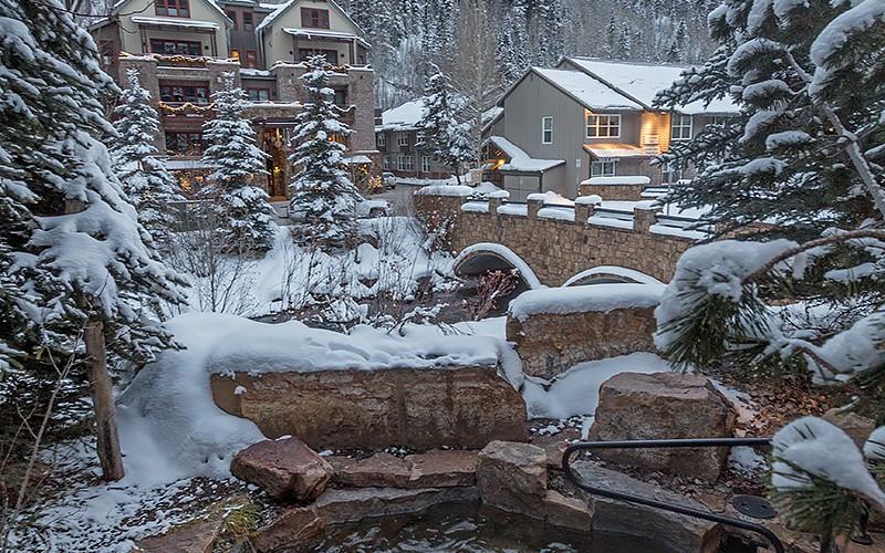 Snow-covered mountain property with stone buildings, evergreens, and a small stream.